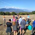 A group of students standing together in discussion on the Greece field class. They are in a large field with a mountain range in the distance.