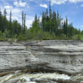 side-on photo of river rapids running through a deep limestone canyon with forest in the background