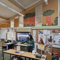 Photograph of an instructor adding water to a bucket as part of a science experience investigating volcanic eruptions. She is stood in a primary school classroom with lots of displays behind her.