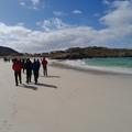 Photograph of students walking along a white sandy beach on the Assynt field class. The sky is blue with small white clouds.