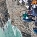 Photograph of demonstrators teaching a group on a field class. They are stood in front of the group, who are sat on a large rock next to the sea,