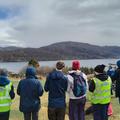 Students overlooking a body of water standing on a hill. They are wearing outdoor gear and high-vis jackets