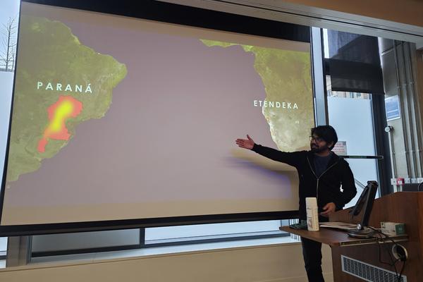 DPhil Conference Presentation Photograph of a DPhil student presenting their work at the graduate conference. They are gesturing at a large screen behind them displaying a map of the South Atlantic Ocean.