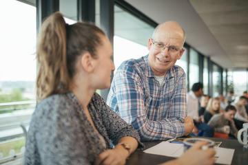 Discussion over Coffee Photograph of staff members in discussion over coffee. They are stood at the end of a bar top in the researcher's common room.