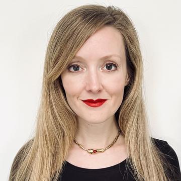 Head and shoulder photograph of Erin Saupe. She has long blonde hair and is wearing a black top. She is wearing red lipstick and smiling at the camera.